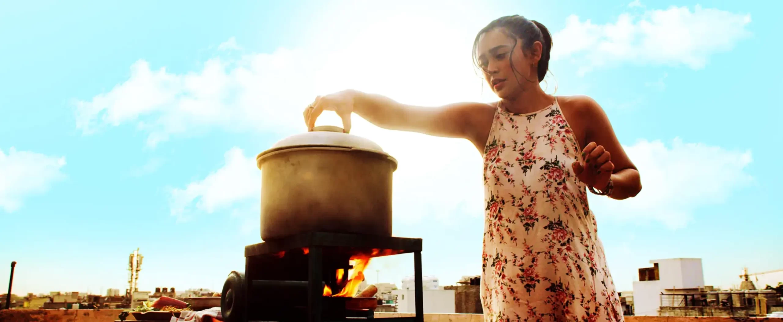 A woman is putting something in a large cookware. She looks worried and is framed against a blue sky with clouds.